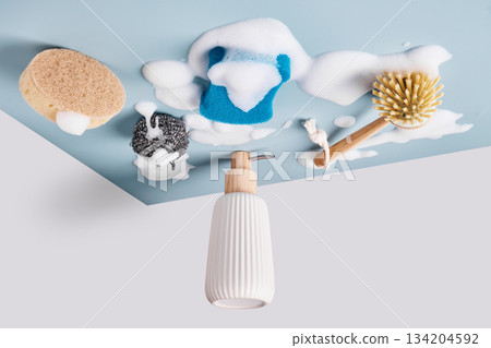 Various cleaning tools covered in white soap foam on light blue background. Inverted image to dishwashing concept Various cleaning tools covered in white soap foam on light blue background. Inverted image to dishwashing concept 134204592
