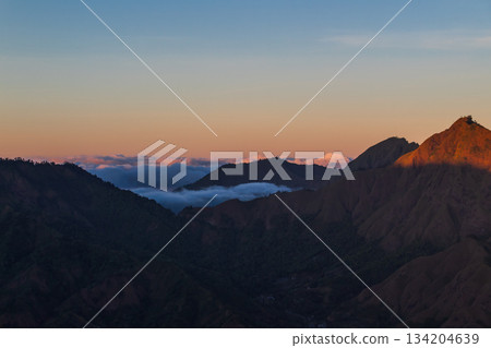 Mountain peaks glowing orange at sunrise over foggy valleys. Mountain peaks glowing orange at sunrise over foggy valleys. 134204639