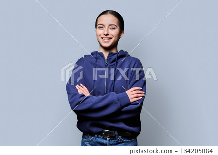 Beautiful young woman with crossed arms looking at camera on grey background Beautiful young woman with crossed arms looking at camera on grey background 134205084