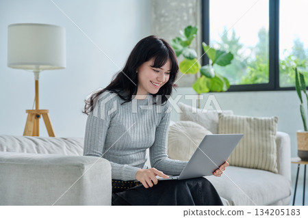 Young woman looking at laptop screen talking having video call sitting on sofa at home 134205183