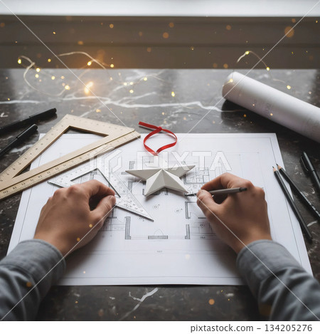 architect's hands drawing a house plan decorated with a white origami star and a christmas ribbon architect's hands drawing a house plan decorated with a white origami star and a christmas ribbon 134205276