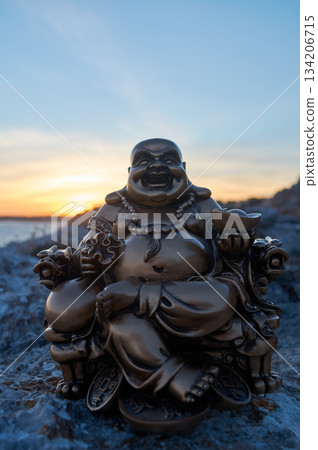 Buddha figure on some rocks, in the sunset, on the sea 134206715