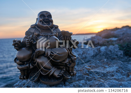 Buddha figure on some rocks, in the sunset, on the sea 134206716