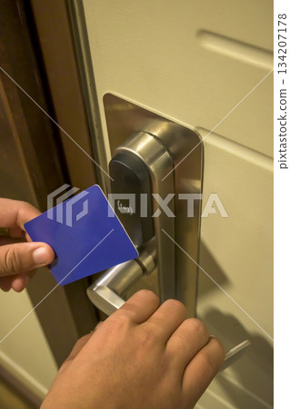 A hand holding a blue card key near a hotel door lock in a long hallway, key electronic lock, hotel room, holidays in mallorca, spain 134207178