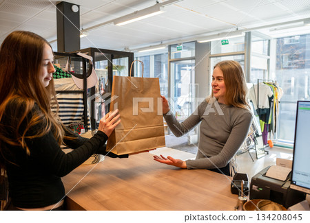 Customer receiving paper bag from shop assistant in secondhand store 134208045