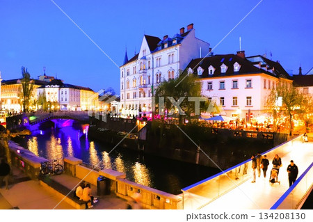 The Ljubljanica River flowing through the city of Ljubljana, the illuminated Ribja Bridge, the Triple Bridge and the surrounding cityscape at night 134208130