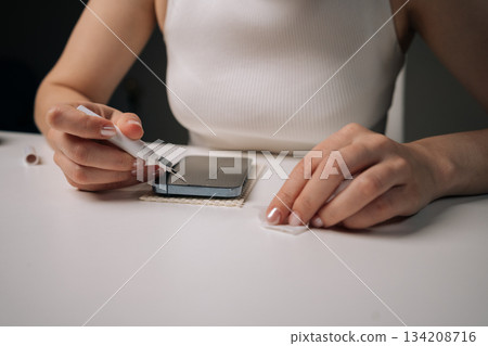 Woman cleaning microphone of smartphone with specialized brush tool, focusing on maintaining optimal audio quality and ensuring hygiene for better communication. Concept of mobile phone service. Woman cleaning microphone of smartphone with specialized brush tool, focusing on maintaining optimal audio quality and ensuring hygiene for better communication. Concept of mobile phone service. 134208716
