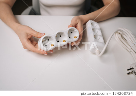 Top view of female professional examining white electrical socket sitting at white desk. Woman holding white triple electrical socket in hands. Concept of electrical installation and home renovation. Top view of female professional examining white electrical socket sitting at white desk. Woman holding white triple electrical socket in hands. Concept of electrical installation and home renovation. 134208724