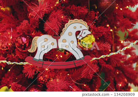 Toy figure of a horse on tree. Toy rocking horse ornament hanging on red Christmas tree with glowing lights. Concept of 2026 Year of Red Fire Horse, celebration and festive symbol of luck Toy figure of a horse on tree. Toy rocking horse ornament hanging on red Christmas tree with glowing lights. Concept of 2026 Year of Red Fire Horse, celebration and festive symbol of luck 134208909