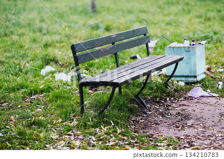 A trash can is positioned right next to a bench that is located in a park. High quality photo A trash can is positioned right next to a bench that is located in a park. High quality photo 134210783