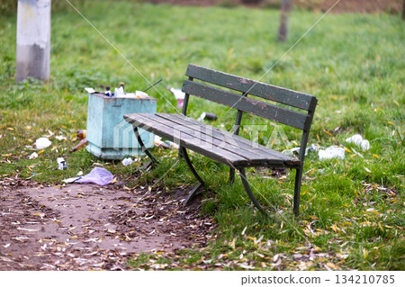 A trash can is positioned right next to a bench that is located in a park. High quality photo A trash can is positioned right next to a bench that is located in a park. High quality photo 134210785