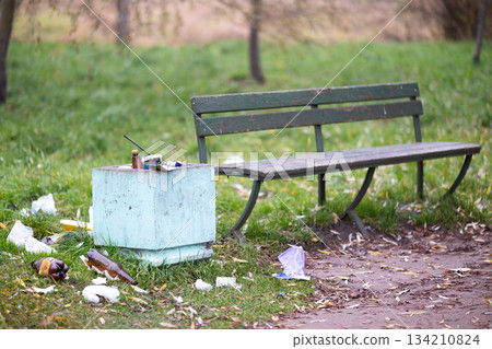 A trash can is positioned right next to a bench that is located in a park. High quality photo 134210824