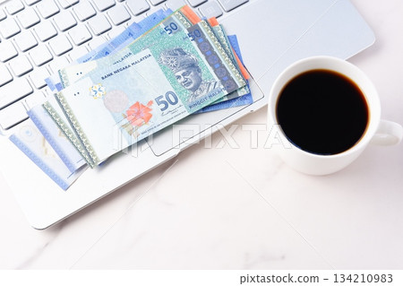 馬來西亞林吉特（MYR）紙鈔、一台筆記型電腦和一個咖啡杯，裡面有現煮的咖啡 134210983