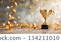 Golden trophy on a reflective surface surrounded by festive confetti and ribbons, symbolizing celebration and achievement in a joyful atmosphere 134211010