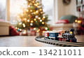 Colorful toy train set on circular tracks, positioned in front of a beautifully decorated Christmas tree, creating a festive holiday atmosphere with warm lights and cozy ambiance 134211011