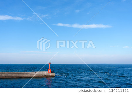 A red navigational marker (lighthouse/beacon) standing against a calm blue sky, sea and horizon 134211531