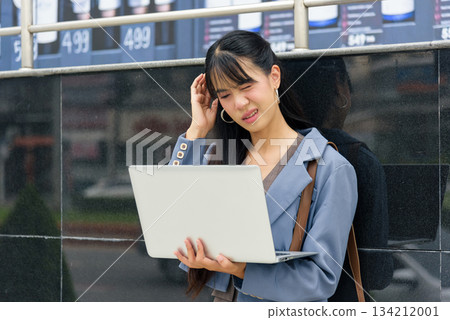 Woman person on street, business work lifestyle outdoors, travel, experiencing stressful headache while holding laptop, feeling unwell in urban city environment, requiring break. Woman person on street, business work lifestyle outdoors, travel, experiencing stressful headache while holding laptop, feeling unwell in urban city environment, requiring break. 134212001