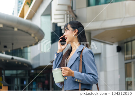 Business woman talks on phone, walks city street outdoor for daily work travel lifestyle, holding insulated drink mug, confident person navigating urban environment, modern architecture. 134212030