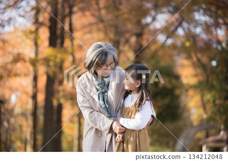 Grandmother and granddaughter playing together in an autumn park with autumn leaves 134212048