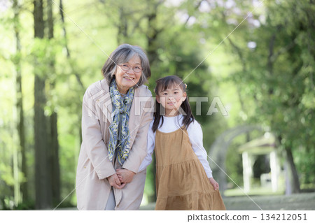 Grandmother playing in a park with fresh greenery in spring and granddaughter cuddling together, looking at the camera Grandmother playing in a park with fresh greenery in spring and granddaughter cuddling together, looking at the camera 134212051