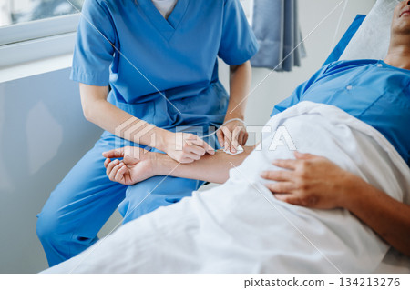 Friendly Female Head Nurse Making Rounds does Checkup on Patient Resting in Bed. She Checks tablet while Man Fully Recovering after Successful Surgery in hospital Friendly Female Head Nurse Making Rounds does Checkup on Patient Resting in Bed. She Checks tablet while Man Fully Recovering after Successful Surgery in hospital 134213276