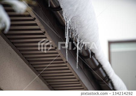 Icicles Hanging From Snow-Covered Roof Edge Create Winter Chill and Quiet Morning Atmosphere Icicles Hanging From Snow-Covered Roof Edge Create Winter Chill and Quiet Morning Atmosphere 134214292