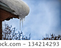 Snow-Capped Roof With Icicles Hanging Over Eaves On A Cold Winter Day 134214293
