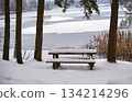 Snow-covered picnic table overlooking a frozen lake in winter 134214296