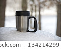 Stainless Steel Travel Mug On Snow in a Quiet Winter Forest Scene 134214299