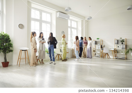 Diverse women standing in bright spacious office, talking during meeting and discussing work issues. 134214398