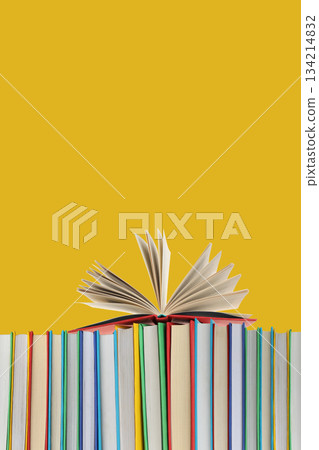 Open book stands on a stack of colorful books against yellow Open book stands on a stack of colorful books against yellow 134214832