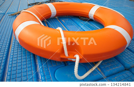 Orange lifebuoy on blue pontoon water safety close up horizontal Orange lifebuoy on blue pontoon water safety close up horizontal 134214841