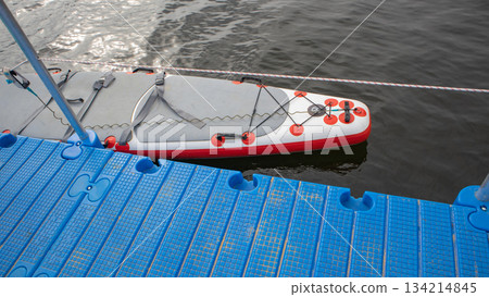 Inflatable SUP board by blue pontoon on water horizontal Inflatable SUP board by blue pontoon on water horizontal 134214845