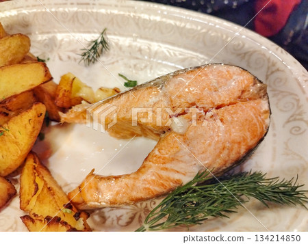 Salmon steak with potato wedges on plate close up horizontal Salmon steak with potato wedges on plate close up horizontal 134214850