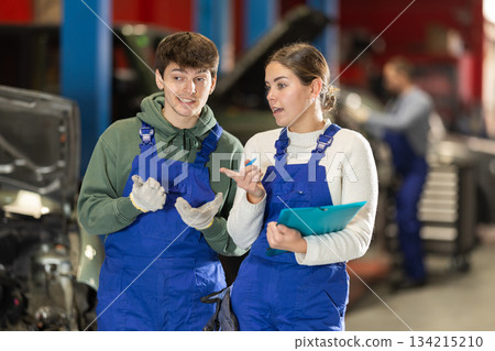 Car service manager discusses car repair problems with mechanic. He takes notes on paper Car service manager discusses car repair problems with mechanic. He takes notes on paper 134215210