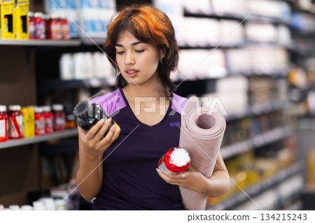 Young girl choosing a bottle of vitamins in sports nutrition store 134215243