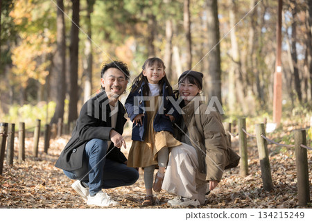 Family playing in a park with roadside trees in autumn and winter. Image of going out and leisure wearing coats. Smiling, full body, looking at the camera. Family playing in a park with roadside trees in autumn and winter. Image of going out and leisure wearing coats. Smiling, full body, looking at the camera. 134215249