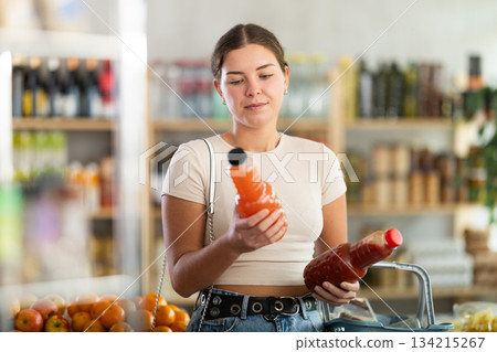 Girl hold packages bottles and choose consider juice in store Girl hold packages bottles and choose consider juice in store 134215267