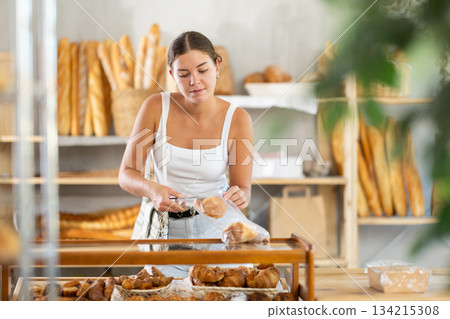 Young woman putting croissants in bag in bakery 134215308