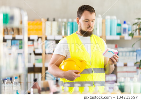 Male builder in yellow vest with helmet in his hands looks for medicine in pharmacy 134215557