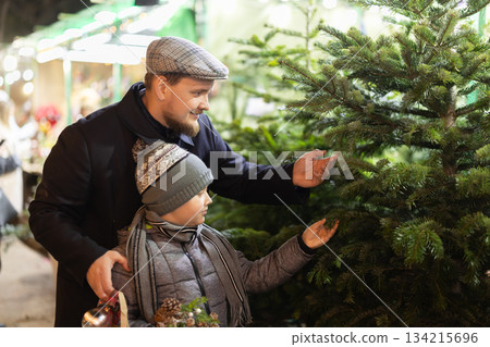 Man and his son at spruce bazaar examines branches of live fir tree. 134215696