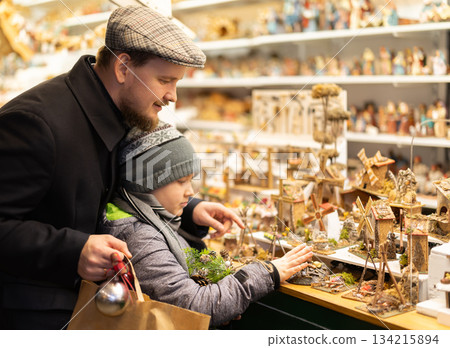 Dad and son standing near counter at Christmas market fair, choosing figurines for nativity scene Dad and son standing near counter at Christmas market fair, choosing figurines for nativity scene 134215894