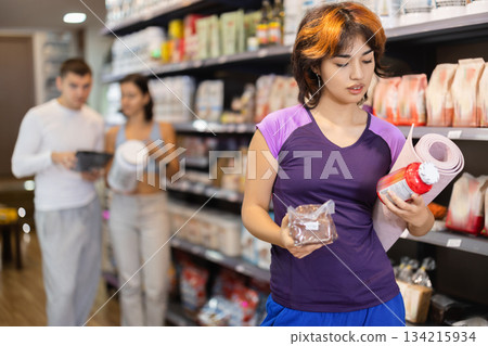 Girl buyer compares glycemic index of bread product and sports nutrition supplement in jar 134215934