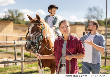 Young woman leading horse with boy on horseback Young woman leading horse with boy on horseback 134215949