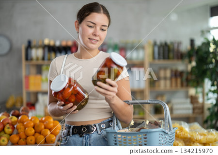 Young woman chooses pickled tomatoes in grocery 134215970