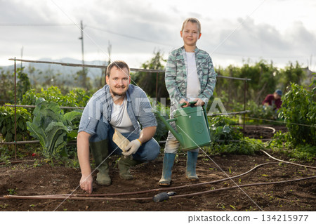 Young man with boy planting seeds in field 134215977