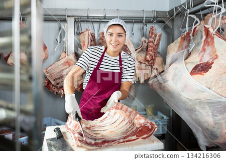 Smiling workwoman cutting beef ribs in meat processing workshop 134216306