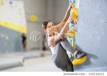 Sportive woman climbing on artificial rock wall in rock climbing gym Sportive woman climbing on artificial rock wall in rock climbing gym 134216321