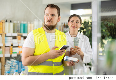 Laborer man builder in pharmacy scans QR code on gel for burns, pharmacist offer help for customer Laborer man builder in pharmacy scans QR code on gel for burns, pharmacist offer help for customer 134216322