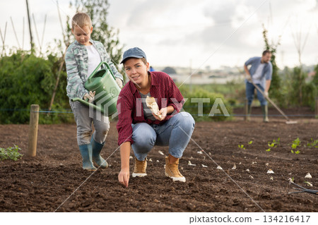 Woman planting seeds boy watering beds Woman planting seeds boy watering beds 134216417